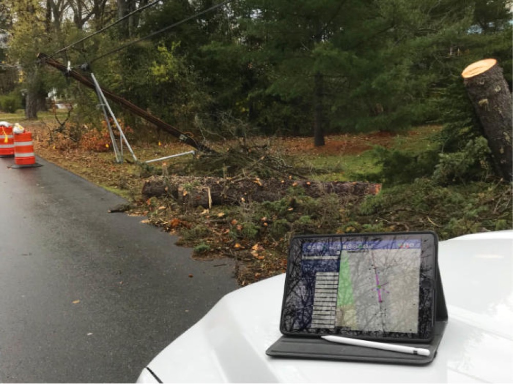 Storm damage assessment: snapped pole and downed tree, with Atlas running on a tablet on the truck hood